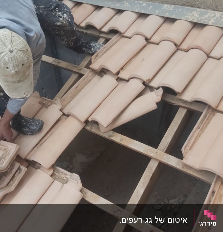 עובד מתקין רעפים על גג עץ